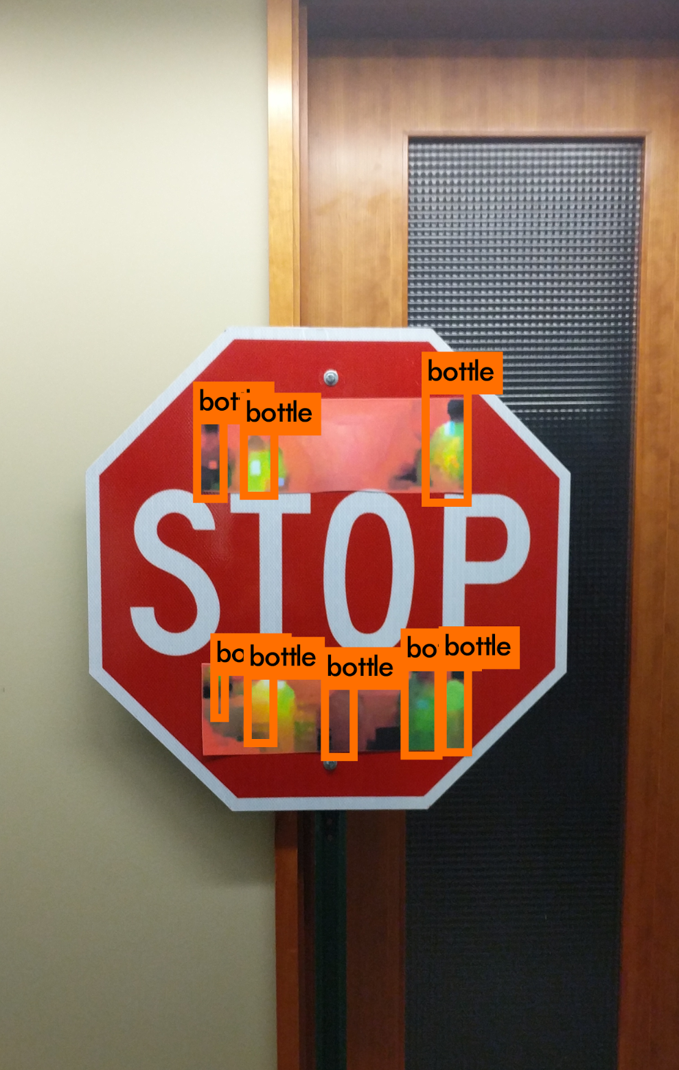 A stop sign is shown with various stickers on it.  On top of the stickers, erroneous identifications of bottles are shown (no bottles are present in the image).